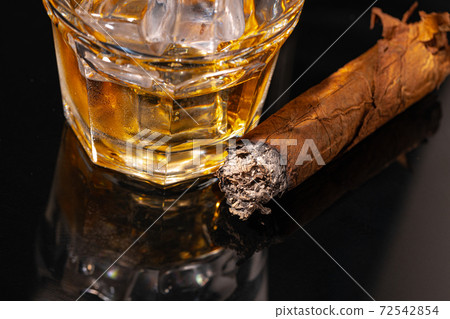 Glass of whisky and lighted cigar on black background 72542854