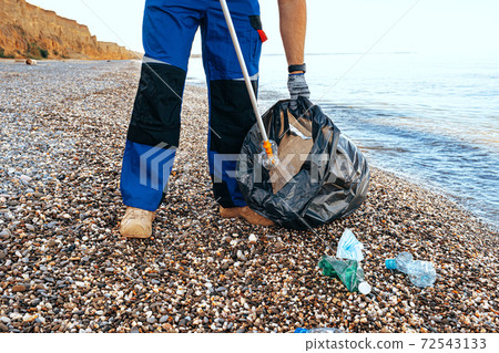 Close up photo of a man collecting garbage with a grabbing tool on the beach Close up photo of a man collecting garbage with a grabbing tool on the beach 72543133