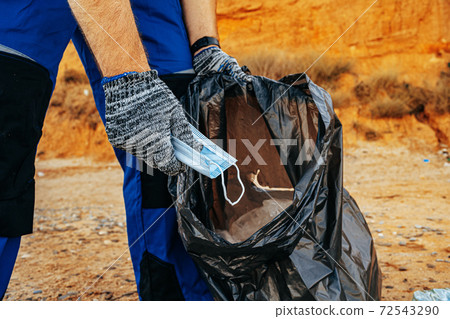 Man volunteer collecting used medical masks on the beach near the ocean Man volunteer collecting used medical masks on the beach near the ocean 72543290