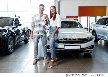 Young happy couple just bought a new car in a dealership Young happy couple just bought a new car in a dealership 72543489