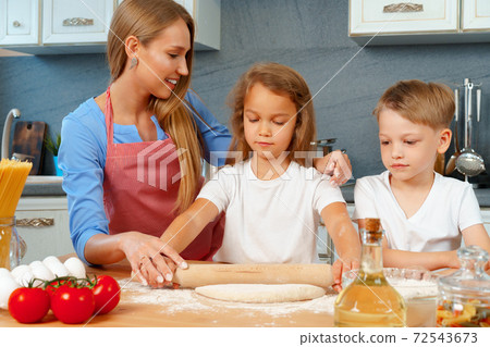 Mother and her little kids, boy and girl, helping her to prepare dough Mother and her little kids, boy and girl, helping her to prepare dough 72543673