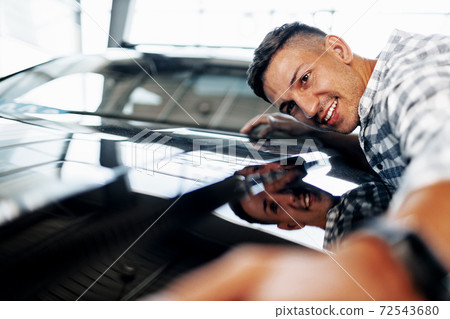 Cheerful young man customer buys a new car in a dealership Cheerful young man customer buys a new car in a dealership 72543680
