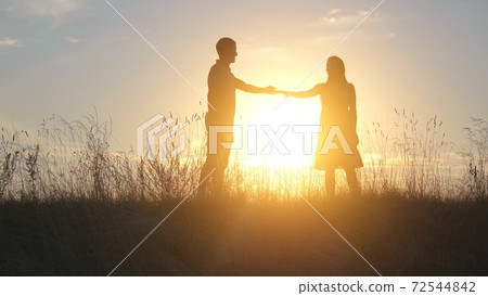 A beautiful young couple at sunset stretch their hands to each other. 72544842