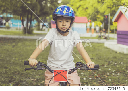 Asian girl learns to ride bike in park. Portrait of a cute kid on bicycle. Asian girl learns to ride bike in park. Portrait of a cute kid on bicycle. 72548343