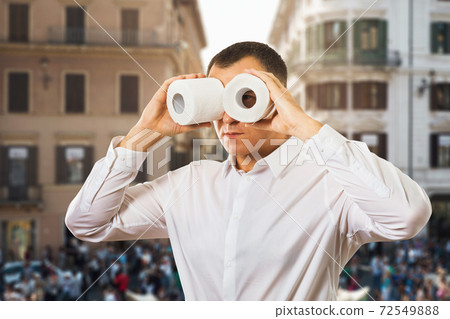 A man on the street looks through toilet paper like binoculars. Concept on the topic of search a toilet A man on the street looks through toilet paper like binoculars. Concept on the topic of search a toilet 72549888