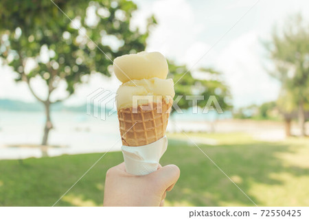 Close up of hand holding mango ice cream with the pool view. Summer time. 72550425