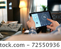 Man is Adjusting a temperature using a tablet with smart home app in modern living room 72550936