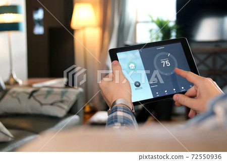 Man is Adjusting a temperature using a tablet with smart home app in modern living room Man is Adjusting a temperature using a tablet with smart home app in modern living room 72550936