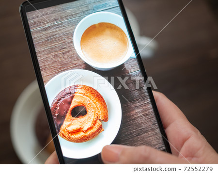 A woman's hand shooting a donut on a table with a smartphone 72552279