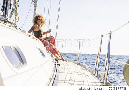 Happy woman enjoy sail boat travel trip sit down on the boat with ocean around - luxury vacation lifestyle for rich people - beautiful curly blonde female traveling outdoor 72552756