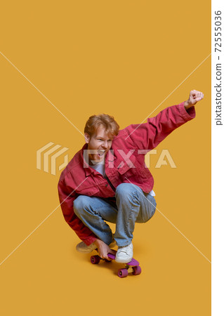 Ginger young man in red jacket jumping on a skateboard 72555036
