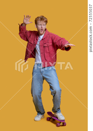Confident ginger young man in red jacket with a skateboard 72555037