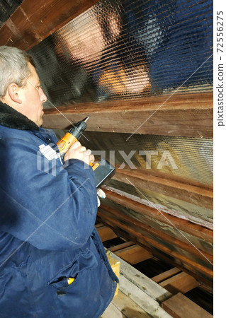 The wizard uses a cordless drill and screw the screws into boards that hold foil film and mineral wool to heal the roof of the house The wizard uses a cordless drill and screw the screws into boards that hold foil film and mineral wool to heal the roof of the house 72556275