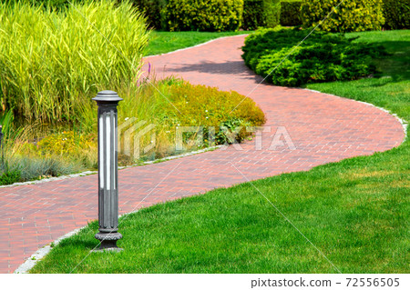 Lighting ground lamp street mounted on a green lawn in a park with winding curved footpath and a green lawn and reeds. Lighting ground lamp street mounted on a green lawn in a park with winding curved footpath and a green lawn and reeds. 72556505