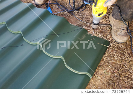 The master drill a hole with a professional drill sheet of metal for mounting on the roof of the house The master drill a hole with a professional drill sheet of metal for mounting on the roof of the house 72556744