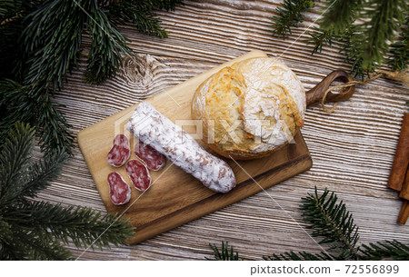 bread and sausage lie on a wooden board. surrounded by fir branches. bread and sausage lie on a wooden board. surrounded by fir branches. 72556899