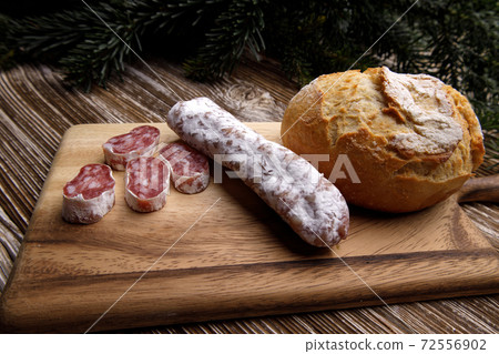 bread and sausage lie on wooden board. in background there are spruce branches bread and sausage lie on wooden board. in background there are spruce branches 72556902