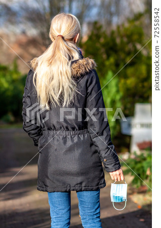 Woman, standing at the grave of family members with a facemask during the pandemic Woman, standing at the grave of family members with a facemask during the pandemic 72558542