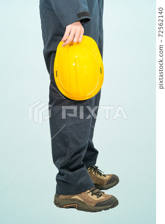 Worker standing in blue coverall holding yellow hardhat 72562140