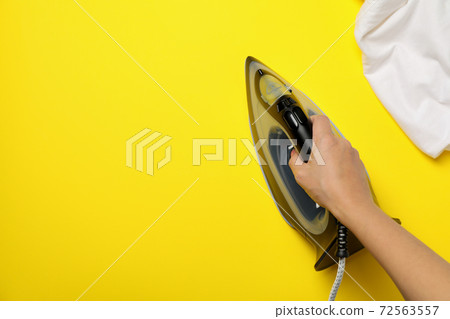 Female hand hold modern iron on yellow background, top view 72563557