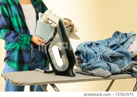Iron on ironing board and woman with basket of laundry 72563575