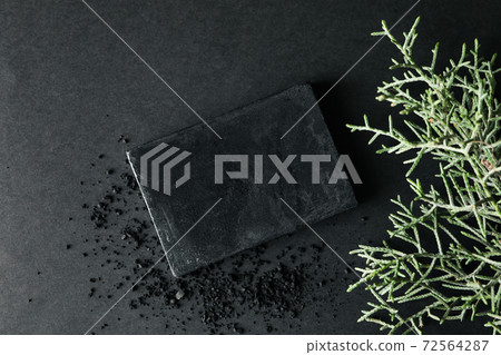 Charcoal soap and thuja branches on black background 72564287