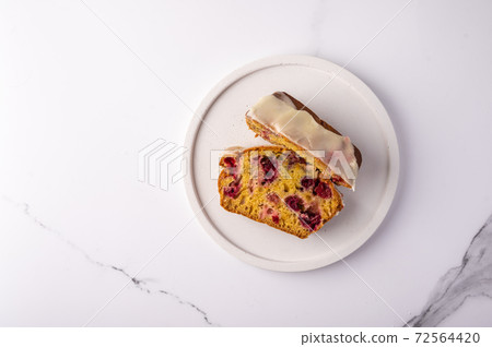 Two pieces of cupcake with cranberries and icing sugar on a white plate on a light background Two pieces of cupcake with cranberries and icing sugar on a white plate on a light background 72564420