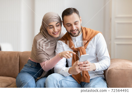 Muslim Couple Using Mobile Phone Sitting On Sofa At Home 72564491