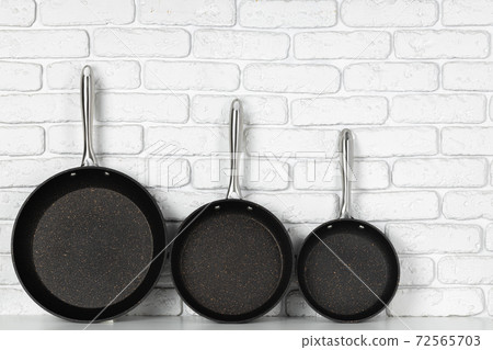 Set of cooking pans against white brick wall 72565703