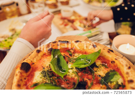 Thin-crust pizza topped with fresh basil leaves. Slices of pizza. Home made food. Italian vegetarian pizza. Concept for a tasty and hearty meal. Rustic wooden background. 72565873