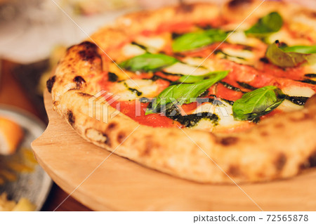 Thin-crust pizza topped with fresh basil leaves. Slices of pizza. Home made food. Italian vegetarian pizza. Concept for a tasty and hearty meal. Rustic wooden background. Thin-crust pizza topped with fresh basil leaves. Slices of pizza. Home made food. Italian vegetarian pizza. Concept for a tasty and hearty meal. Rustic wooden background. 72565878