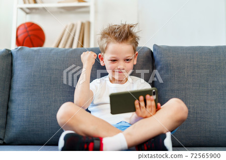 Little boy sitting on sofa at home and using smartphone 72565900