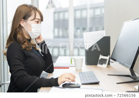 一個戴著口罩和在辦公室裡操作電腦的女人 72566156