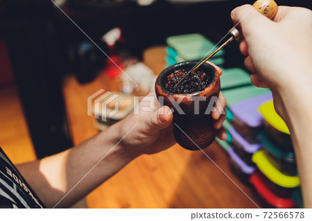 Preparing hookah for smoking, filling clay bowl with tobacco, male hands visible. Preparing hookah for smoking, filling clay bowl with tobacco, male hands visible. 72566578