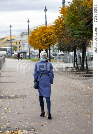 Woman walks on the asphalt with yellow leaves. 72566898