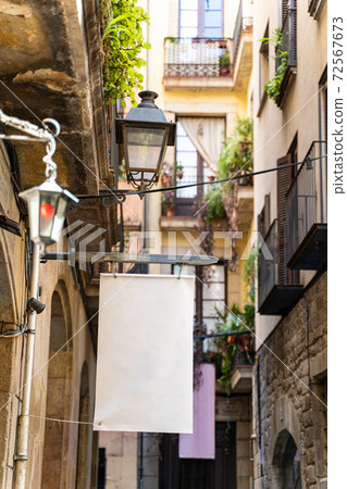 Narrow street with old historic houses and white empty billboards in Barcelona 72567673