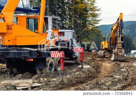 Heavy industrial machinery vehicles working in mud dirt bog road on top of mountain peak resort in forest. Crane and excavator digger at construction site and building of new ski lift station Heavy industrial machinery vehicles working in mud dirt bog road on top of mountain peak resort in forest. Crane and excavator digger at construction site and building of new ski lift station 72568941