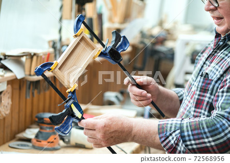 Senior carpenter glueing wooden craft surface and joining with clamps. Woodwork carpenter with equipment and tools at workshop. Handmade diy furniture.Wood part glue joiner 72568956