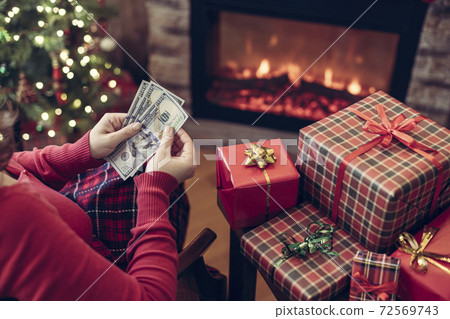 Christmas. Woman in sweater using tablet for searching gift ideas sitting at table near fireplace and christmas tree.  72569743