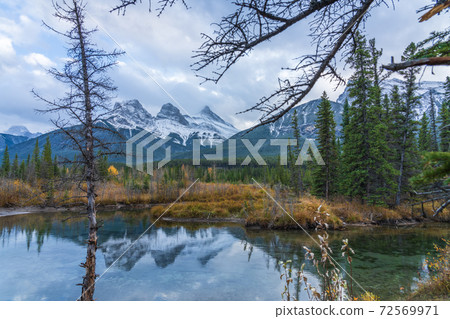 Snow capped The Three Sisters trio peaks mountain with blue sky and white clouds reflect on water surface in autumn. Beautiful natural scenery landscape at Canmore, Canadian Rockies, Alberta, Canada. 72569971