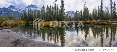 Snow capped Mount Lawrence Grassi mountain with blue sky and white clouds reflect on water surface in autumn. Beautiful natural scenery landscape at Canmore, Canadian Rockies, Alberta, Canada. 72569972