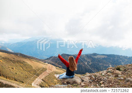Young woman is sitting on the cliff of the mountain in Sochi, Russia. Young woman is sitting on the cliff of the mountain in Sochi, Russia. 72571262