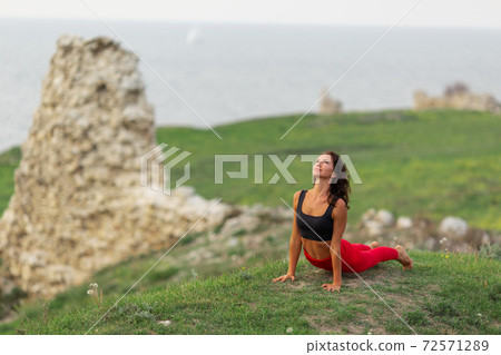 Pretty woman is wearing sportive clothes doing yoga exercises in the park. 72571289