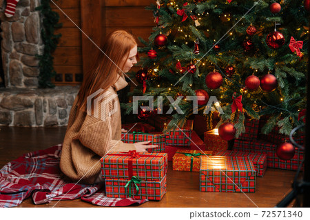 Beautiful happy smiling young woman putting Christmas gift under the xmas tree at cozy living room. Beautiful happy smiling young woman putting Christmas gift under the xmas tree at cozy living room. 72571340
