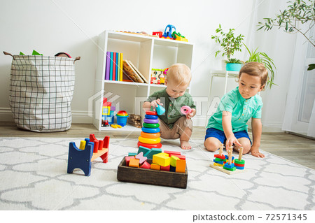 Children playing with wooden toys sitting on a floor Children playing with wooden toys sitting on a floor 72571345