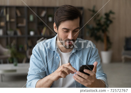 Stunned young man shocked by good news on smartphone Stunned young man shocked by good news on smartphone 72572767