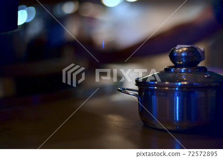 A steel pan with a closed lid on the table stands alone against a backdrop of light bokeh in a catering restaurant. 72572895