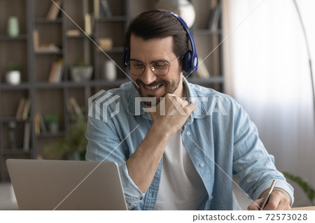 Happy man in headphones work on laptop online 72573028