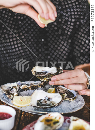 Woman putting lemon juice to fresh Irish oysters Woman putting lemon juice to fresh Irish oysters 72573375