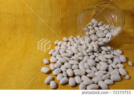 White dry beans in a jar lies spilled out on a yellow lemon background with a copy of the space White dry beans in a jar lies spilled out on a yellow lemon background with a copy of the space 72573753